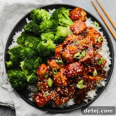 A square image depicting a bountiful serving of crispy teriyaki tofu over white rice, accompanied by abundant broccoli florets.