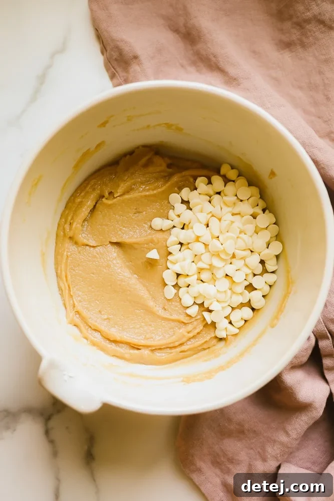 White bowl with light brown blondie batter and numerous vegan white chocolate chips ready to be folded in