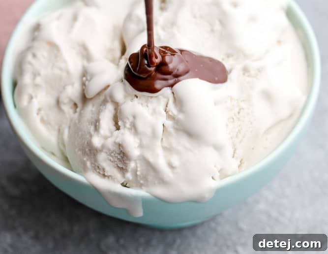 Rich vegan hot fudge being generously drizzled over a scoop of vanilla ice cream in a vibrant teal bowl, creating luscious chocolate ribbons.