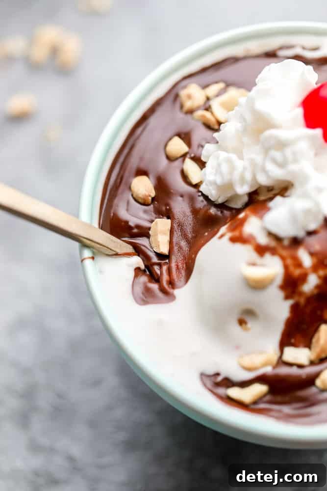 Close-up shot emphasizing the thick, glossy texture of vegan hot fudge coating vanilla ice cream, ready to be enjoyed.