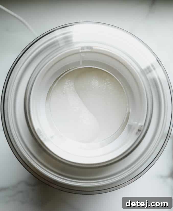 An overhead view of an ice cream maker with a swirling, creamy white mixture inside, resembling soft-serve ice cream.