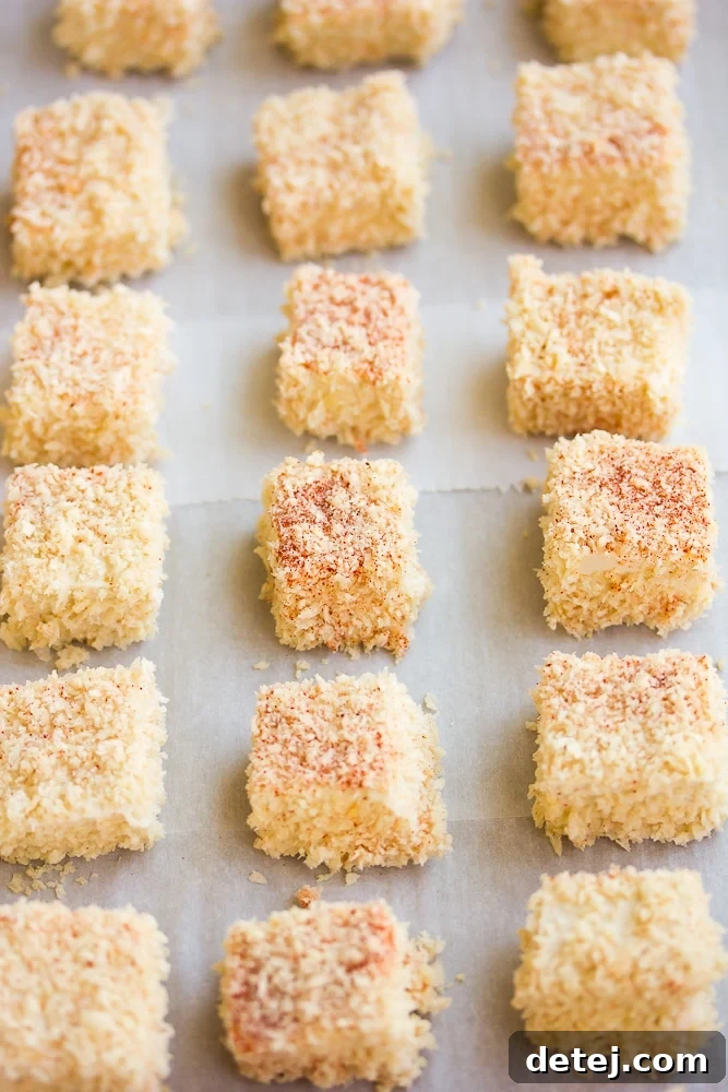 Uncooked, breaded tofu nuggets arranged neatly on a baking sheet lined with parchment paper, ready for baking.