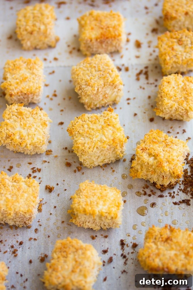 A close-up shot of several crispy, golden-brown tofu nuggets cooling on a baking pan after being baked.