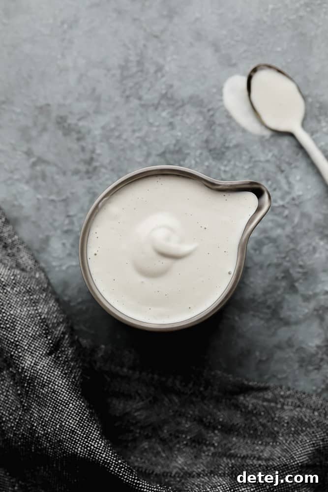 Close-up shot of a grey pitcher filled with creamy vegan heavy cream, with a golden spoon in the background.
