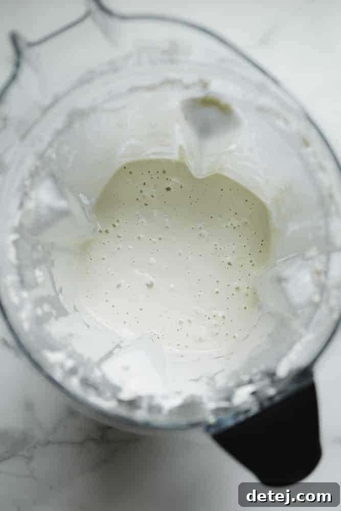 Blended cashews and water resembling thick, white cream inside a blender jar.