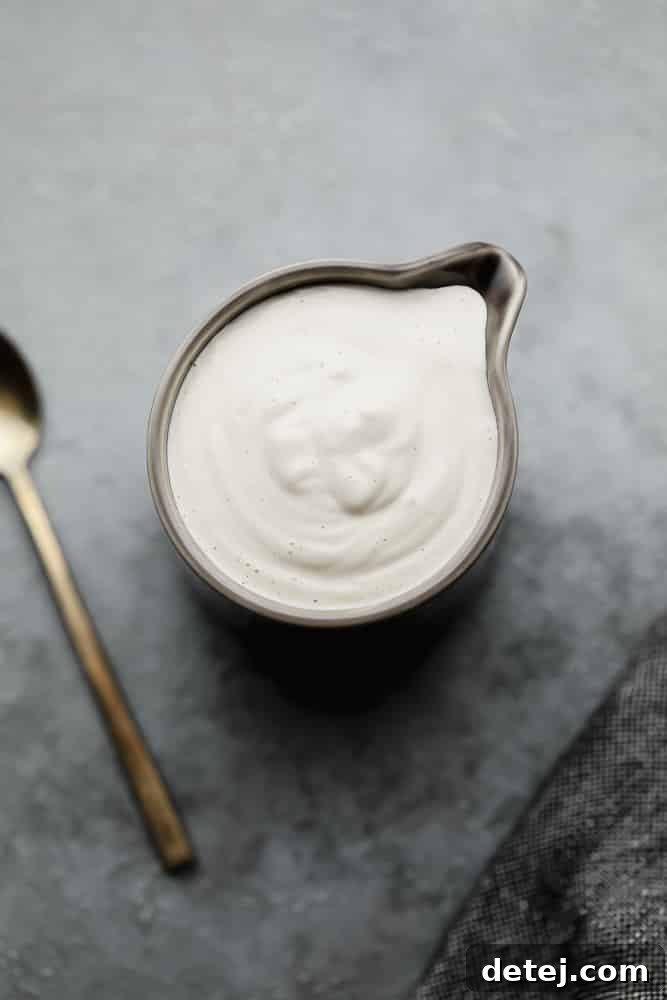 A small, dark grey pitcher elegantly holding a generous amount of creamy white vegan heavy cream.