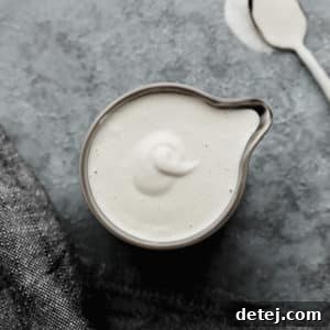 A square image featuring a grey pitcher filled with smooth, white vegan heavy cream, ready for use.