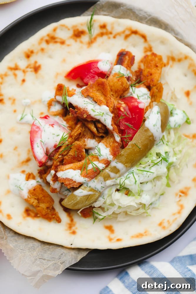 A vibrant Vegan Shawarma wrap, showcasing a generous pile of fresh lettuce, tangy pickles, richly seasoned soy curls, and ripe tomatoes, all nestled in the center of a soft, round flatbread, ready to be folded.