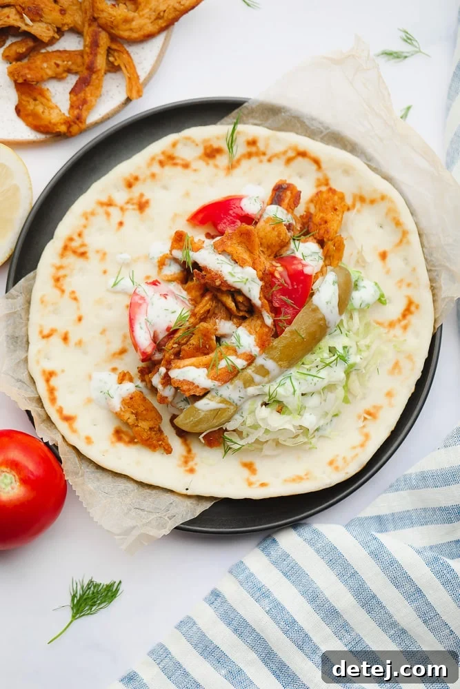 A beautifully presented Vegan Shawarma, featuring a generous assortment of crisp lettuce, tangy dill pickles, richly seasoned soy curls, and ripe tomato slices, artfully arranged on a soft, round flatbread, inviting you to create your perfect wrap.