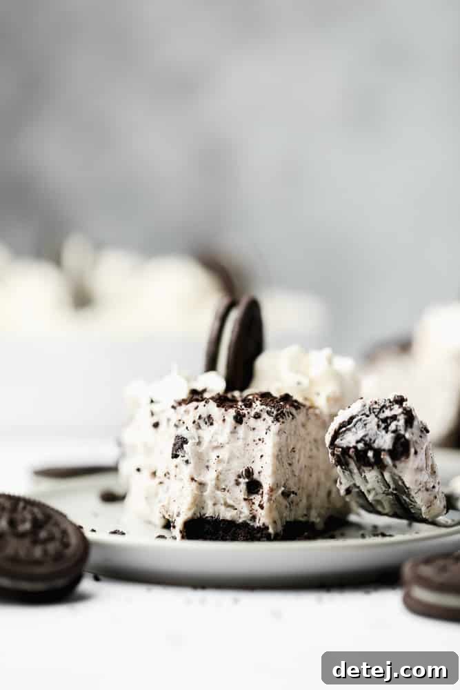 A fork taking a delightful bite from a slice of creamy Vegan Oreo Cheesecake, beautifully presented on a pristine white plate.