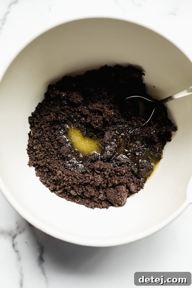 Stirring crumbled dark brown cookies and melted vegan butter together in a white bowl to create the cheesecake crust mixture.