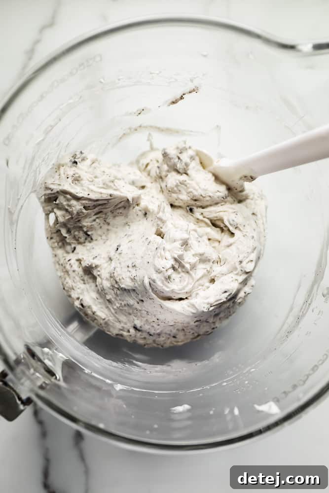 A white spatula stirring a rich cookies and cream mixture in a clear glass bowl, showcasing the decadent filling.