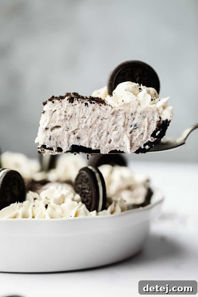 A slice of creamy Vegan Oreo Cheesecake being carefully lifted out of a white pie pan, revealing its perfect layers.