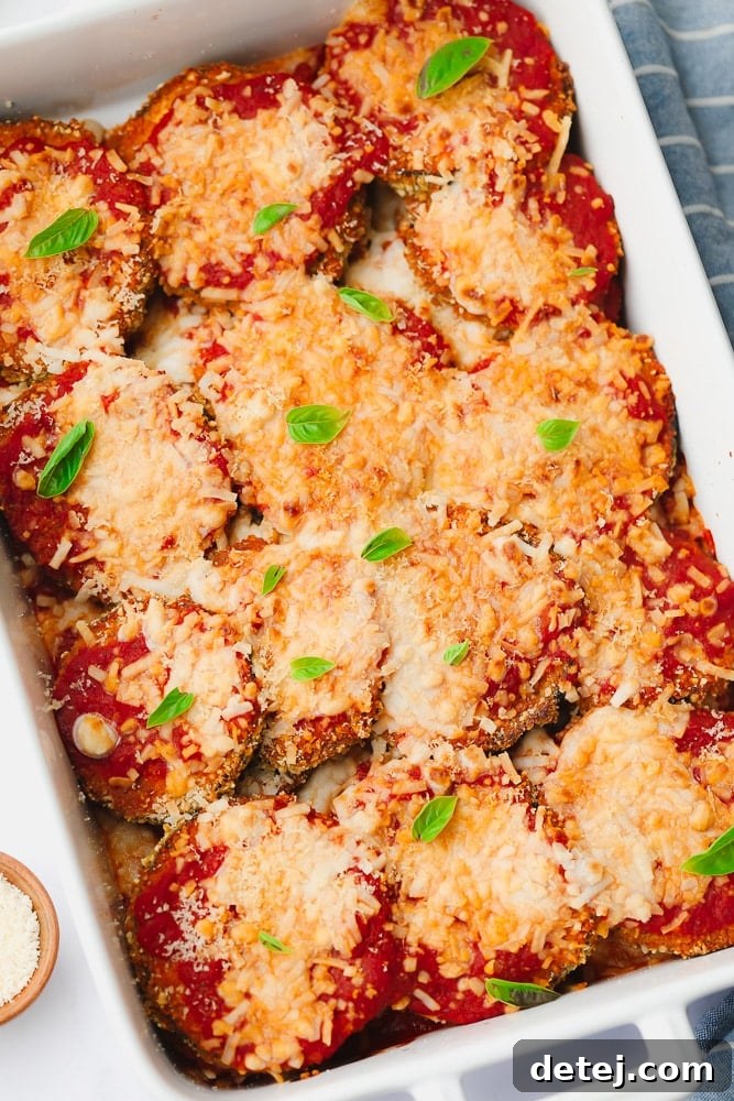 Baked eggplant slices with rich red marinara sauce and perfectly melted white vegan cheese in a pristine white baking dish, ready for serving.