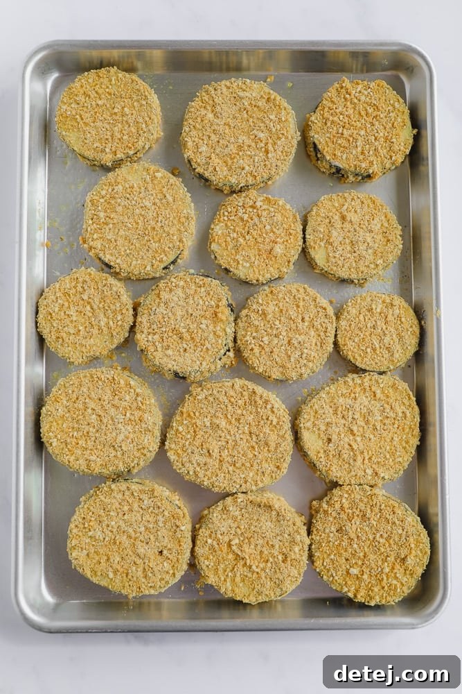 Rows of perfectly coated eggplant slices arranged neatly in a single layer on a baking tray, glistening and ready to be baked to a golden crisp.