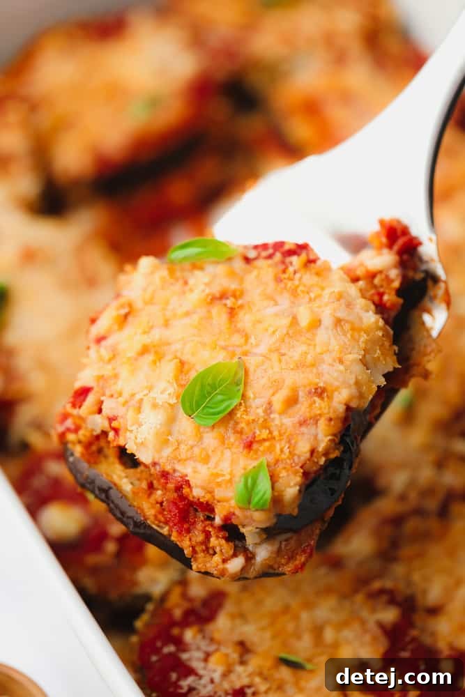 A close-up view of a scoop of vegan eggplant parmesan, showcasing its melted cheese, rich red sauce, and fresh green herbs on top, ready to be enjoyed.