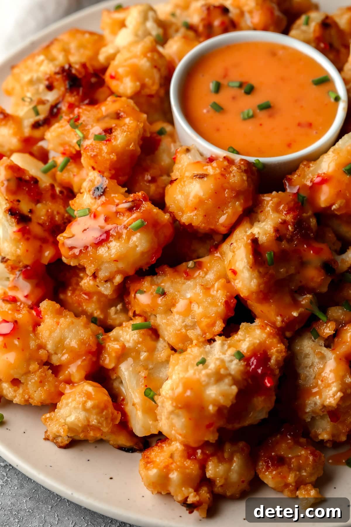 lots of bang bang cauliflower on a plate with more sauce in a little cup