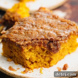 Close-up on a square slice of orange pumpkin coffee cake on a white plate with streusel and glaze.