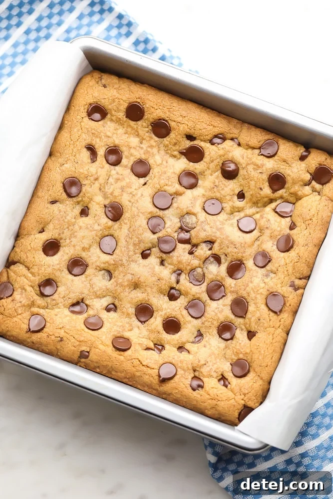 Uncut baked vegan chocolate chip cookie bars still in the baking pan, with a blue kitchen towel visible in the background, ready to be sliced.