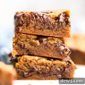 A square photo of three perfectly stacked vegan chocolate chip cookie bars, showing their soft texture and abundant chocolate chips.