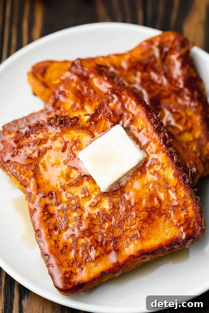 Two slices of golden-brown vegan pumpkin French toast on a white plate, elegantly topped with a square of melting vegan butter, ready to be enjoyed.
