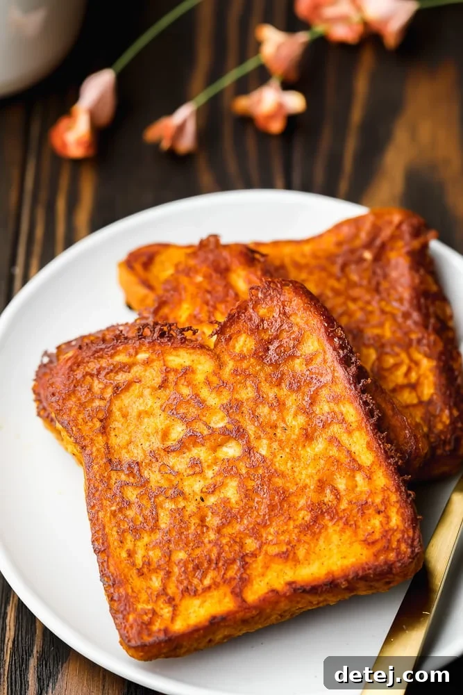 Two perfectly cooked slices of vegan pumpkin French toast, served on a pristine white plate, showcasing their golden-brown exterior and inviting texture.