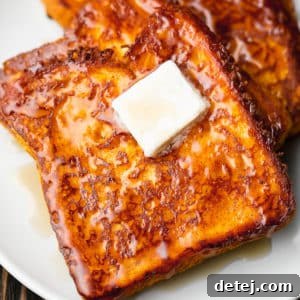 Close-up on a slice of vegan pumpkin French toast on a white plate, beautifully topped with a square of vegan butter, highlighting its rich texture.