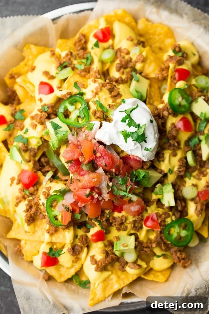 A vibrant plate of ultimate fully loaded vegan nachos, generously topped with an array of fresh ingredients and creamy sauces.