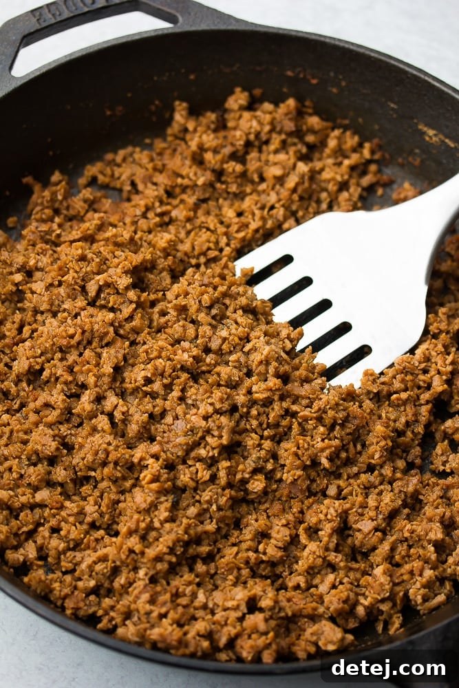 Close-up of savory TVP vegan ground 'beef' sizzling in a black skillet with a spatula, ready for nacho topping.