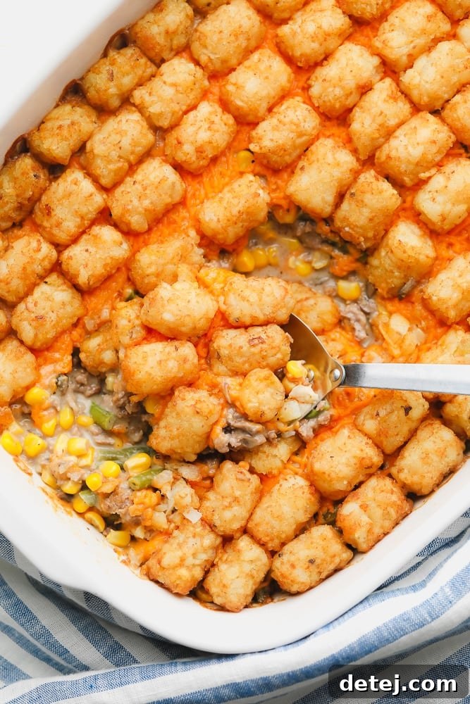 metal spoon scooping some baked tater tot casserole out of a white casserole dish.