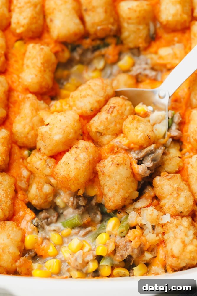 metal spoon scooping some baked tater tot casserole out of a white casserole dish.