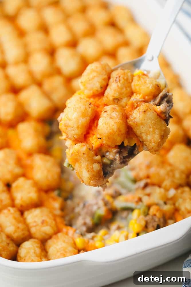 close up on a metal spoon holding a scoop of a baked tater tot casserole.
