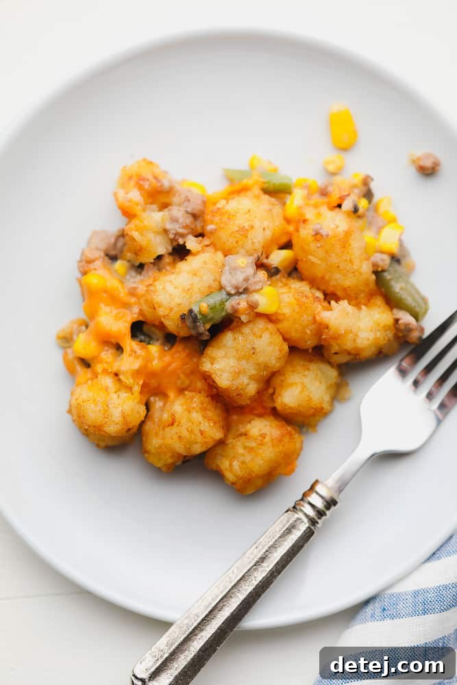 scoop of baked tater tots, corn, and green beans on a white plate next to a fork.