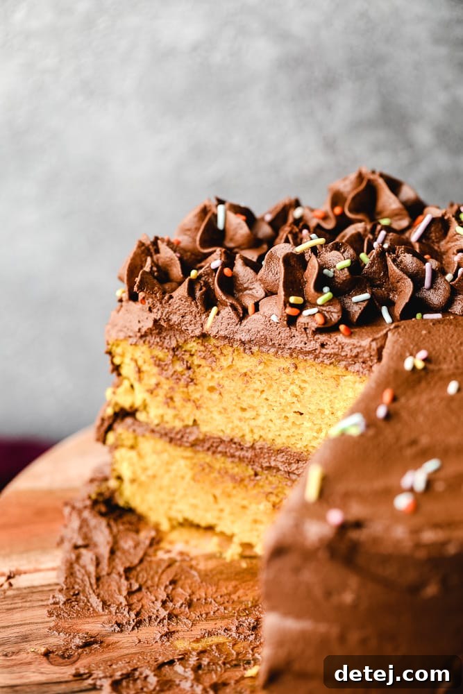 A beautifully sliced vegan yellow cake with chocolate frosting on a rustic wooden board, ready for a party.