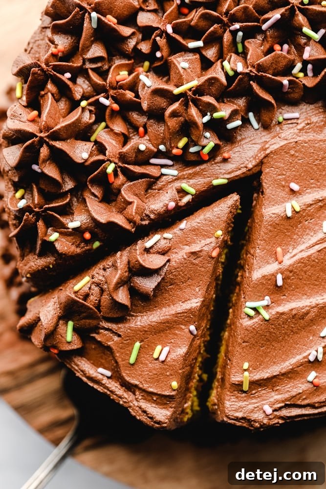 A hand gently removing a slice from a tall, chocolate-frosted vegan yellow cake.