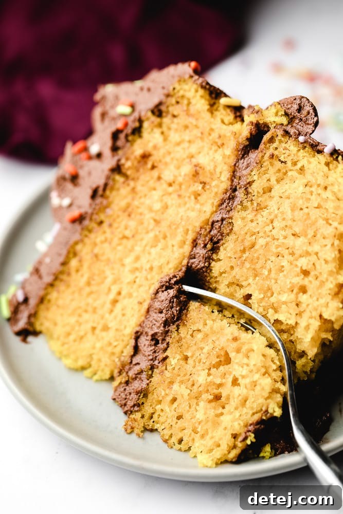 A fork taking a bite out of a perfectly moist slice of vegan yellow cake on a white plate.
