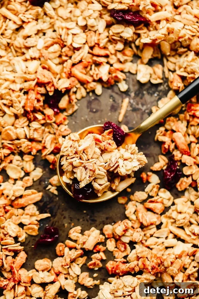A spoonful of golden brown homemade vegan granola, with more granola scattered on a baking sheet.