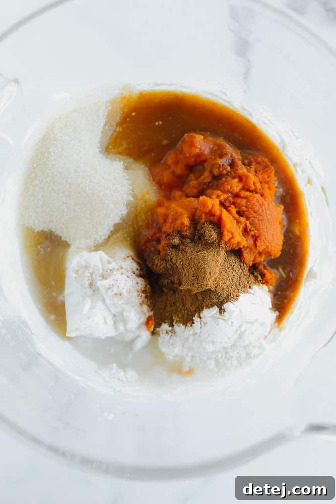 pumpkin puree, sugar, coconut cream, liquid, and spices in a pile in a glass bowl.