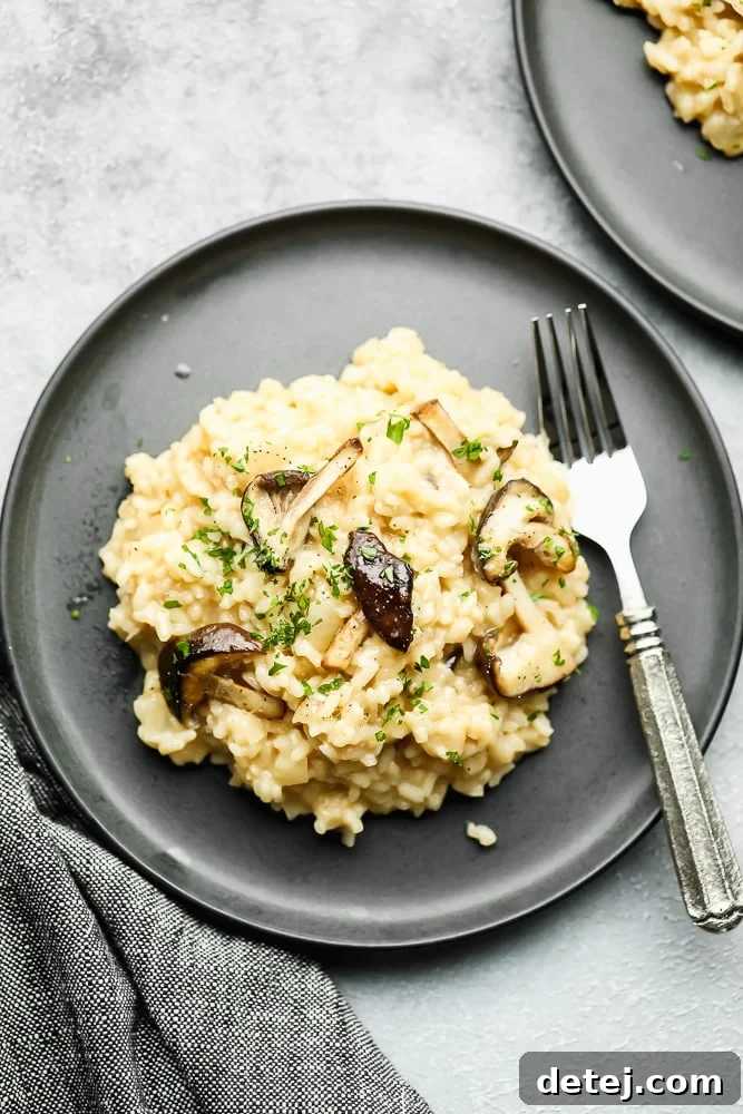 a scoop of creamy risotto topped with cooked mushrooms on a grey plate with a fork.