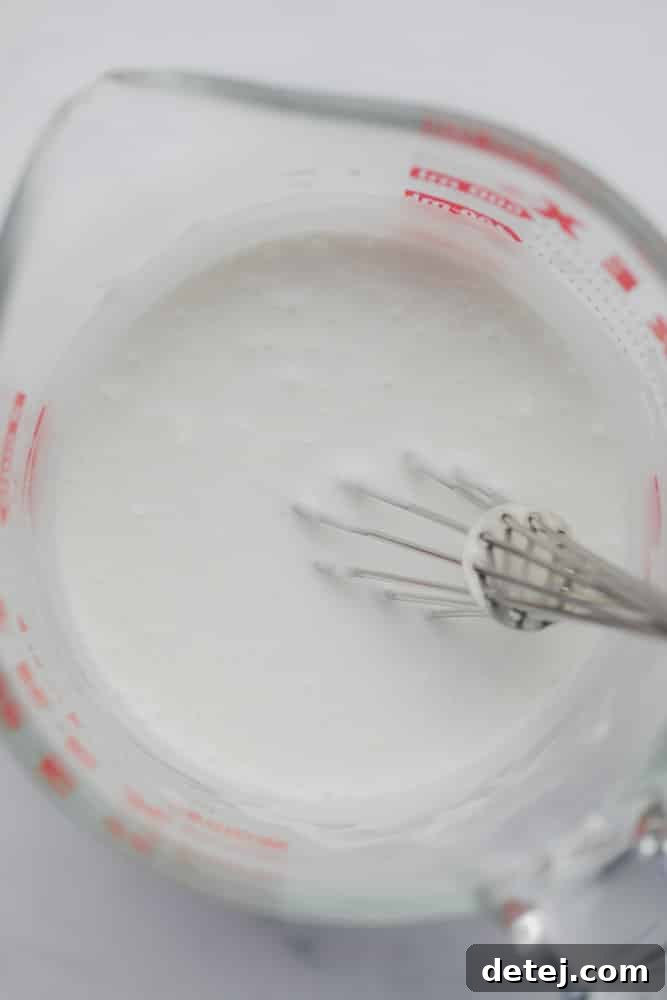 Whisking coconut milk and cornstarch in a clear glass measuring cup.