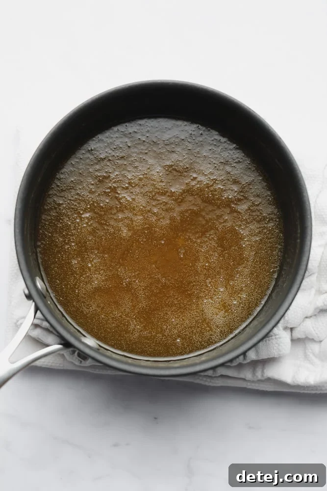 A thin golden-brown caramel sauce simmering in a black saucepan, ready for cooling.
