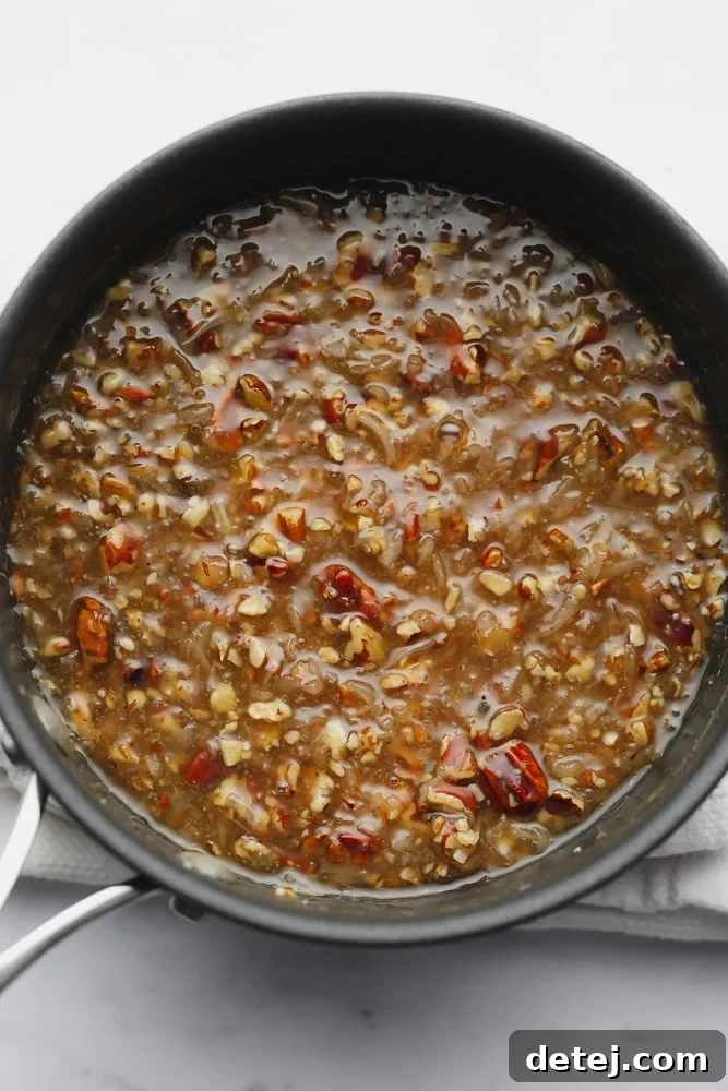 A brown caramel liquid with pecans and coconut cooling in a black pot, thickening.