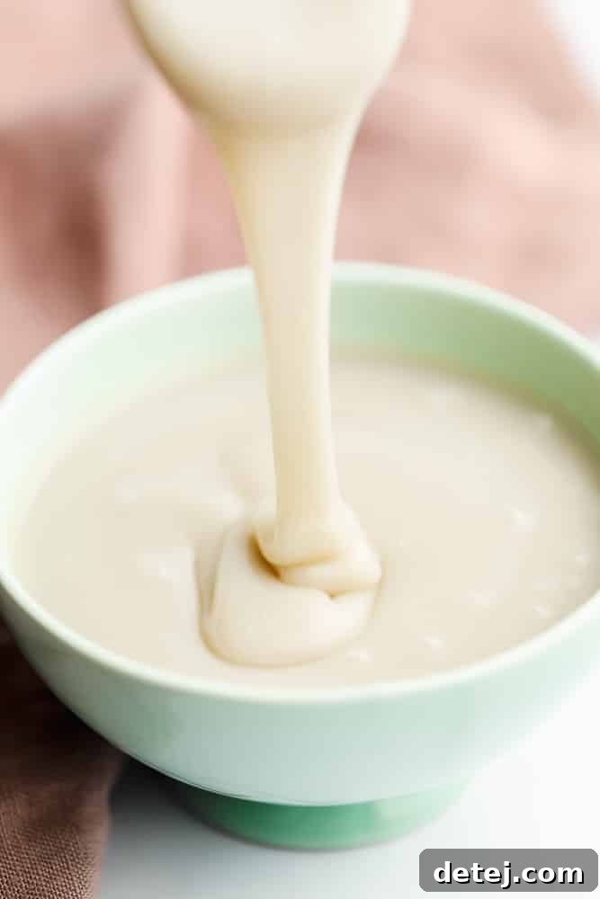 Pouring a creamy white liquid into a green bowl, highlighting the luscious texture of vegan condensed milk.