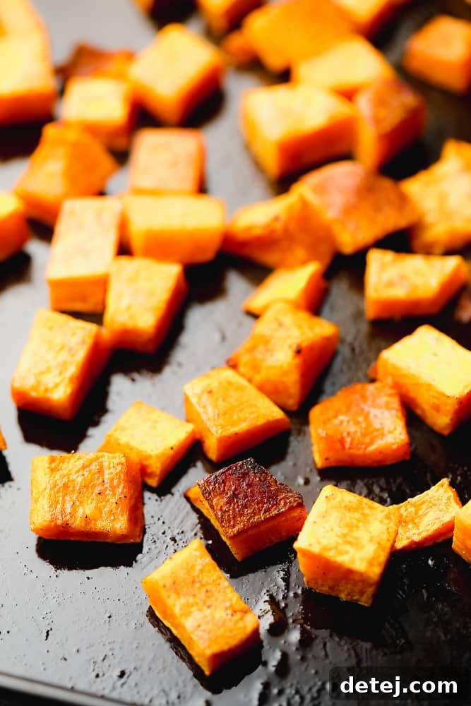 close up on roasted butternut squash cubes on a black baking sheet.