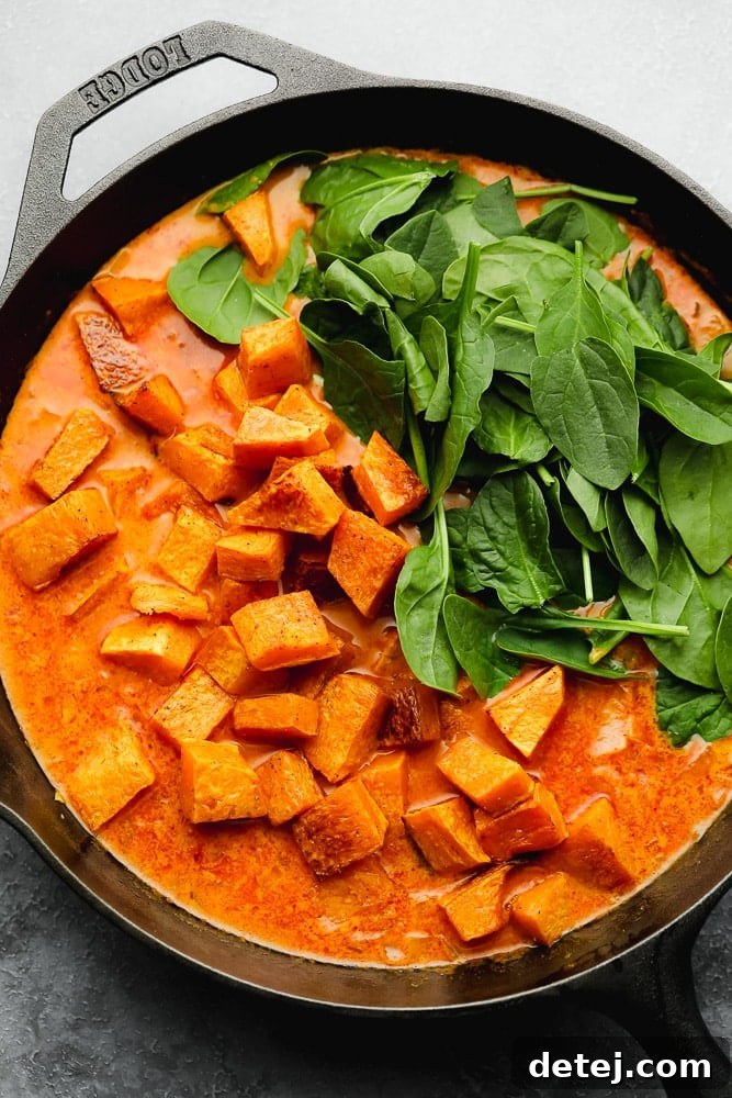 roasted sweet potato cubes and raw spinach on top of an orange liquid in a black skillet.