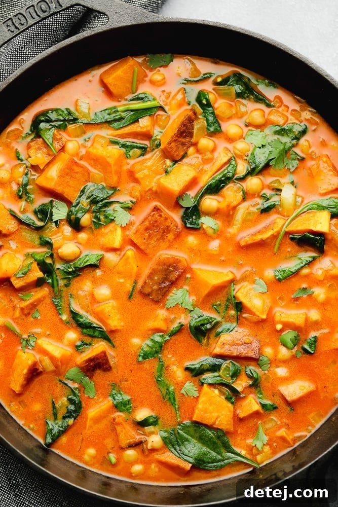 wilted spinach, cubed butternut squash, and chickpeas in an orange liquid in a black skillet.