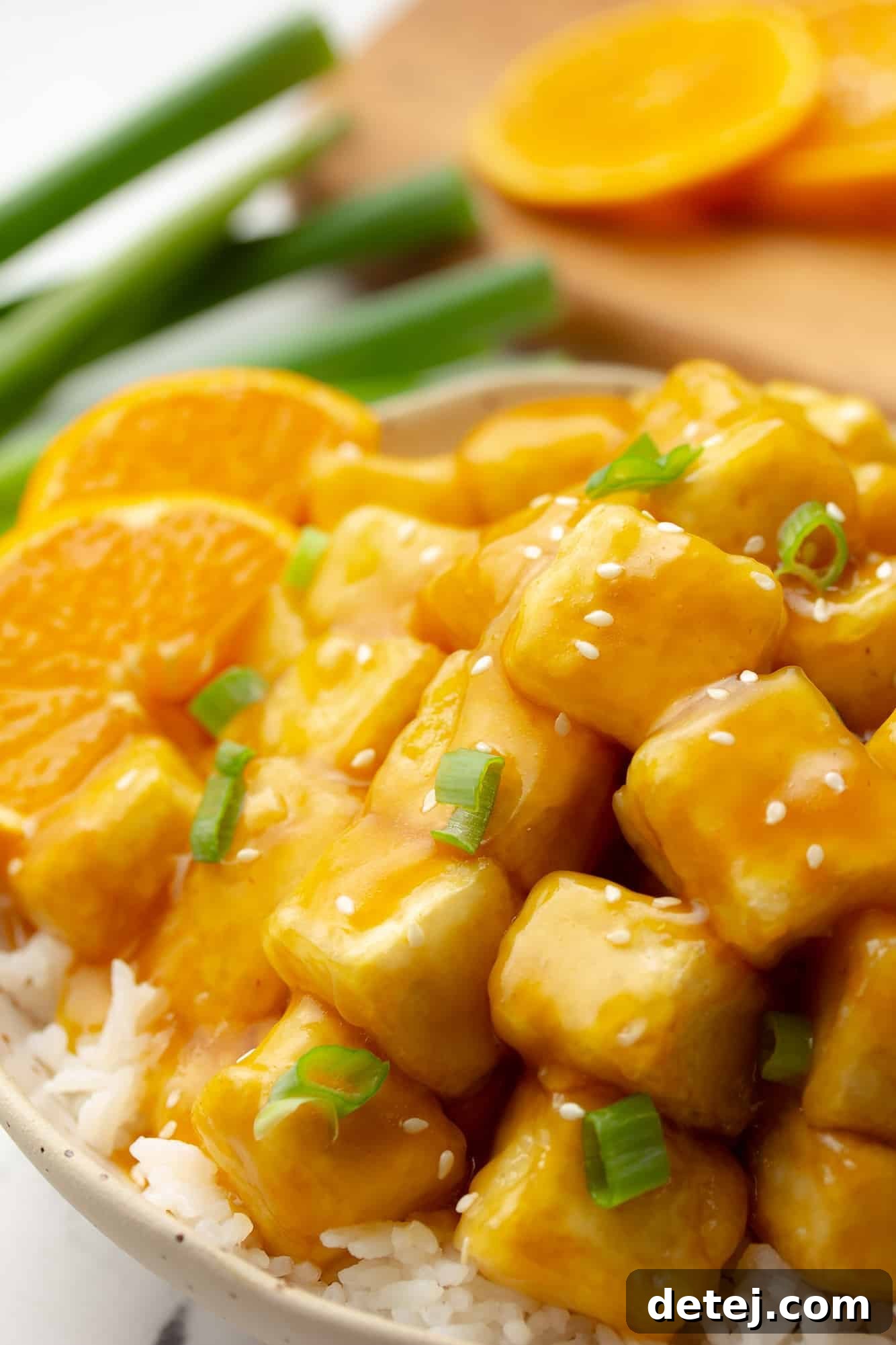 Close up on crispy orange tofu garnished with fresh orange slices and chopped green onions, served as a delicious vegan meal.