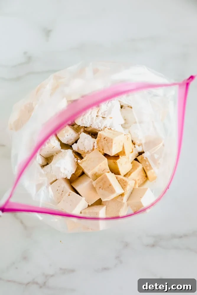 Tofu cubes being coated with cornstarch in a large ziplock bag, a crucial step for achieving crispy texture in orange tofu.