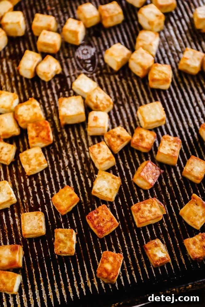 Golden-brown, crispy baked tofu cubes arranged on a parchment-lined baking sheet, ready for the orange sauce.