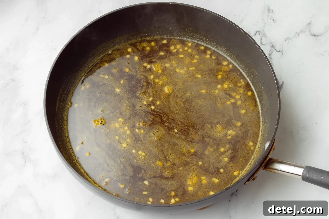 Rich, glossy orange sauce bubbling in a large black skillet, ready to coat the crispy tofu.